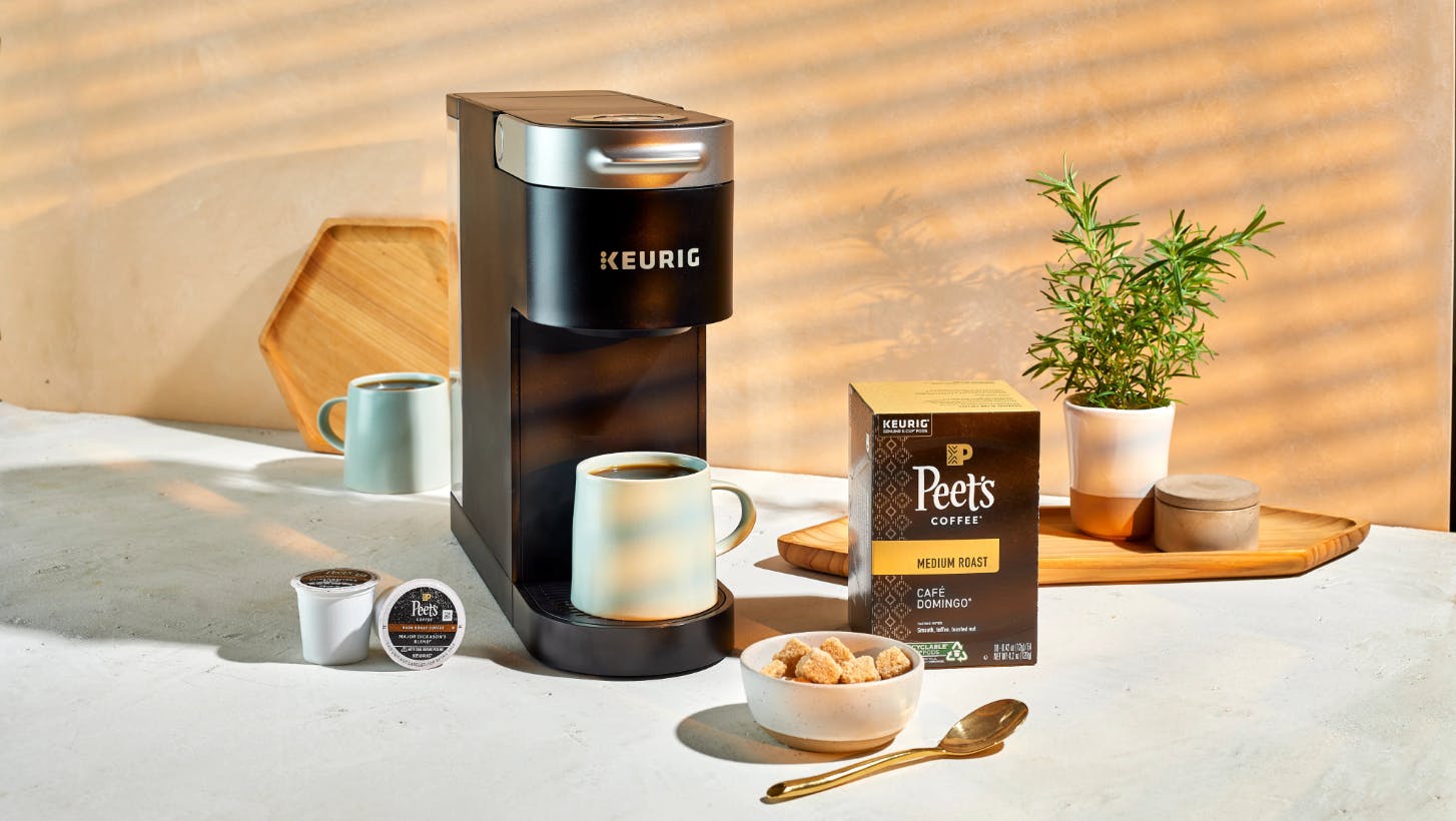 A box of Peet's Cafe Domingo Medium Roast K-Cup Pods sitting on a countertop with a coffee machine